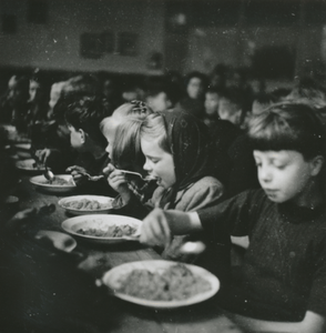876783 Afbeelding van een grote groep kinderen die aan het eten is in een klaslokaal van de Piusschool (Oudegracht 33) ...